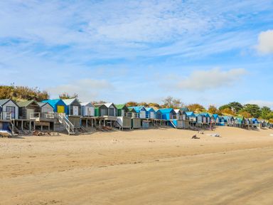 A row of small colorful beach huts on a sandy beach with a blue sky at The Warren D26 in Abersoch