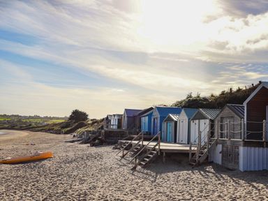 A row of beach huts with stairs on a sandy beach with a kayak on the sand at The Warren D26 in Abersoch
