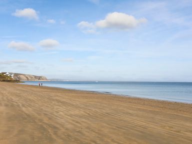 A sandy beach with two people walking near the shoreline and houses on the left at The Warren D26 in Abersoch