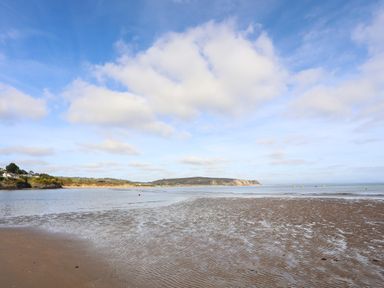 A beach with wet sand and shallow water under a blue sky with clouds at The Warren D26 in Abersoch