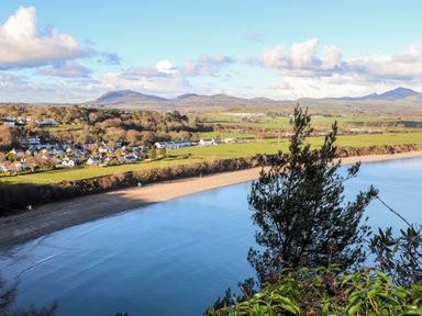 A coastal landscape showing a beach, a bay with water, houses, green fields, hills, and trees at The Warren D26 in Abersoch