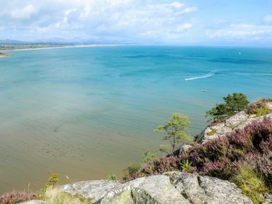 A coastal landscape with rocks and trees overlooking the sea with boats and a distant shoreline at The Warren D26 in Abersoch