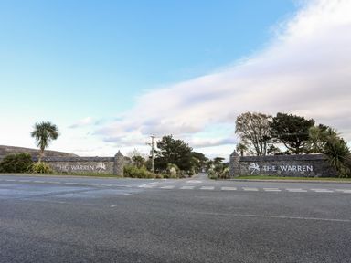 Entrance to a property with stone walls and signs saying The Warren with trees and sky at The Warren D26 in Abersoch
