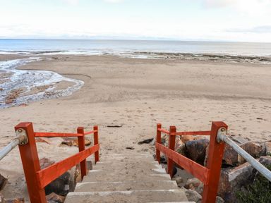 Concrete steps with red railings leading down to a sandy beach and calm sea at The Warren D26 in Abersoch