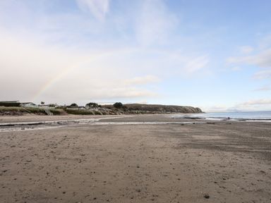 A sandy beach with a rainbow over houses and hills by the sea at The Warren D26 in Abersoch