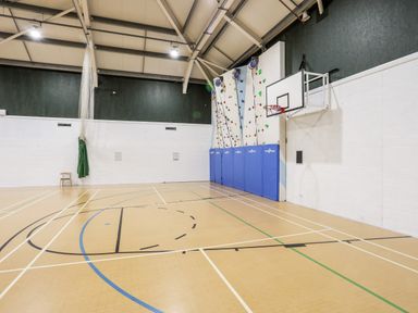 An indoor sports hall with a basketball hoop rock climbing wall and safety mats at The Warren D26 in Abersoch