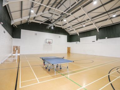 An indoor sports hall with a basketball hoop two small soccer goals and a table tennis table at The Warren D26 in Abersoch