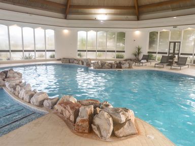 An indoor pool with rocks around the edge and lounge chairs near large windows at The Warren D26 in Abersoch