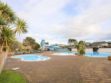 An outdoor pool area with a water slide palm trees and lounge chairs at The Warren D26 in Abersoch