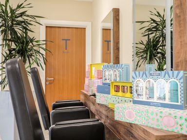 A room with black chairs wooden counter with skincare product boxes and a door labeled team with plants nearby at The Warren D26 in Abersoch