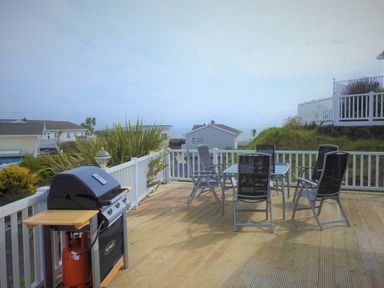 An outdoor patio with a gas grill and a table with six chairs on a wooden deck at The Warren D26 in Abersoch