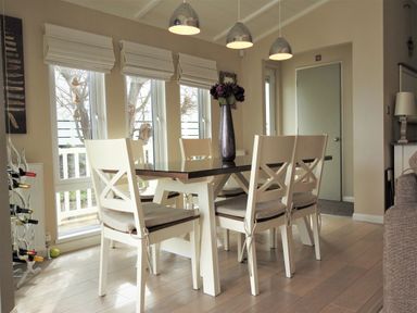 A dining room with six chairs around a table and a vase with flowers on the table at The Warren D26 in Abersoch