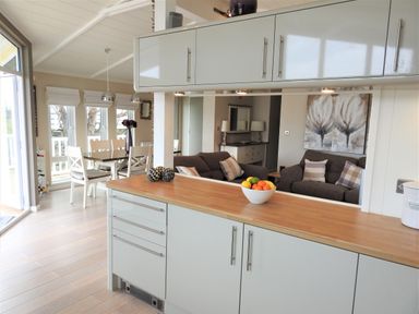 A kitchen with cabinets and a wooden countertop with a bowl of fruit overlooking a living area with sofas and a dining table at The Warren D26 in Abersoch