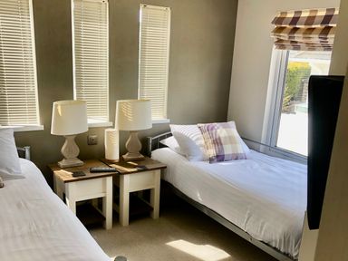 A bedroom with two single beds a window with blinds bedside tables with lamps at The Warren D26 in Abersoch