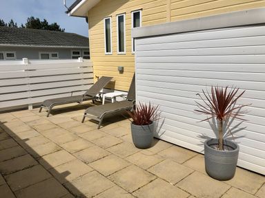 An outdoor patio with two lounge chairs a small white table two potted plants and a white fence at The Warren D26 in Abersoch