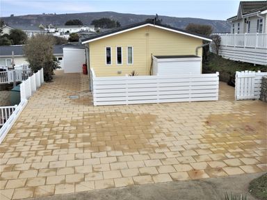 A paved driveway and a yellow house with white fencing and gate at The Warren D26 in Abersoch