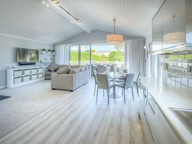 An open plan living room dining area and kitchen with a grey sofa dining table and chairs at The Warren Q4 in Abersoch