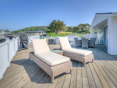 An outdoor deck with two lounge chairs a dining table with chairs and a barbecue grill at The Warren Q4 in Abersoch