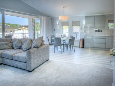 An open living space with a grey sofa dining table with chairs and a kitchen area at The Warren Q4 in Abersoch
