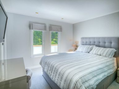 A bedroom with a double bed facing two windows and a bedside table with a lamp at The Warren Q4 in Abersoch