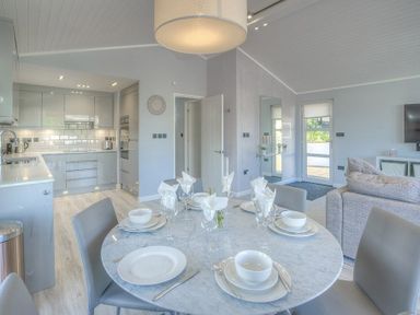 An open dining and kitchen area with a round table set for four people a sofa and wall mounted tv at The Warren Q4 in Abersoch