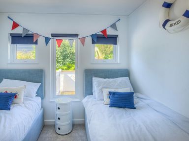 A bedroom with two single beds a storage unit and triangular bunting at The Warren Q4 in Abersoch