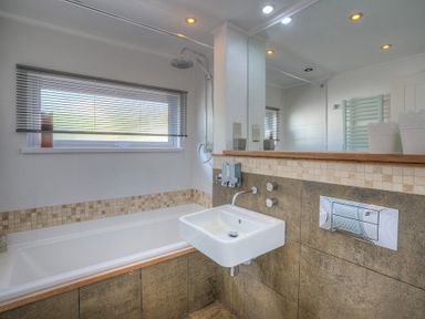 A bathroom with a bathtub shower sink and large mirror at The Warren Q4 in Abersoch
