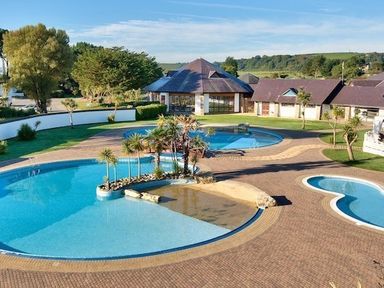 An outdoor area with multiple swimming pools surrounded by trees and buildings at The Warren Q4 in Abersoch