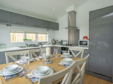 A kitchen with a dining table set with glassware and plates next to grey cabinets and appliances at The Warren T23 in Abersoch