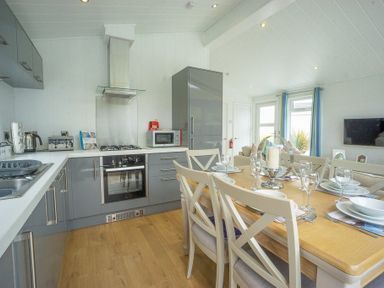 A kitchen and dining area with grey cabinets a dining table set for six and a living area with windows at The Warren T23 in Abersoch