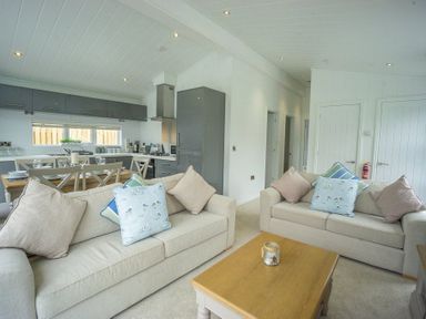 A living room with two beige sofas and a wooden coffee table in an open plan kitchen and dining area at The Warren T23 in Abersoch