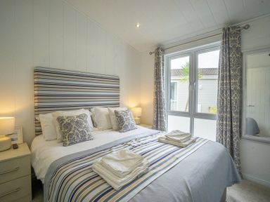 A bedroom with a double bed striped headboard bedside tables lamps and patterned curtains at The Warren T23 in Abersoch