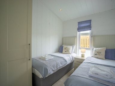 A bedroom with two single beds a nightstand and a window with a blind at The Warren T23 in Abersoch