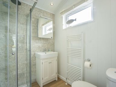 A bathroom with a shower enclosure a sink with cabinet a mirror a window a towel radiator and a toilet at The Warren T23 in Abersoch