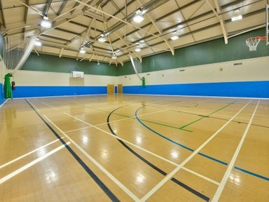 An indoor basketball court with wooden flooring and basketball hoops at each end at The Warren T23 in Abersoch