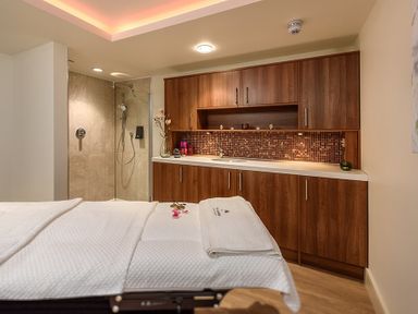 A massage or treatment room with a white treatment bed wooden cabinets and a shower area at The Warren T23 in Abersoch
