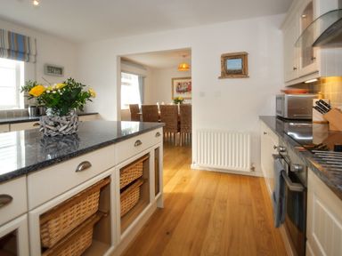 A kitchen with wooden floor granite countertops dining area with wicker chairs in the background at Ty Coed in Abersoch