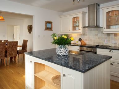 A kitchen with a granite island countertop and a dining area with wicker chairs at Ty Coed in Abersoch