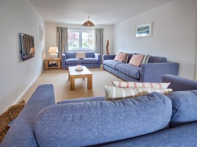A living room with blue sofas and wooden table near a window at Ty Coed in Abersoch