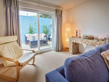 A living room with a cream armchair blue sofa stone mantel and sliding glass doors to outdoor seating at Ty Coed in Abersoch