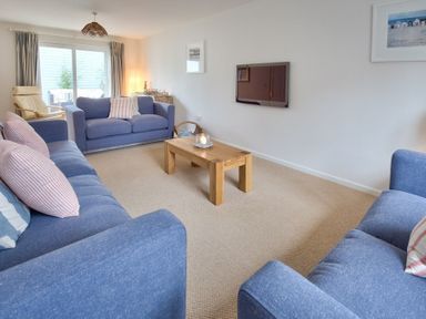 A living room with blue sofas a wooden coffee table a wall-mounted TV and sliding glass doors at Ty Coed in Abersoch