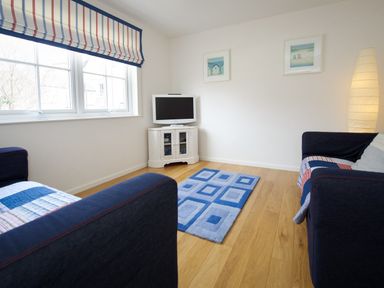 A sitting room with two sofas a small television on a cabinet and a blue rug on wooden floor at Ty Coed in Abersoch