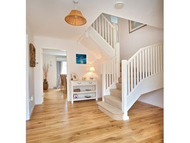 An entry hallway with wooden flooring a white staircase and a white console table with decor at Ty Coed in Abersoch