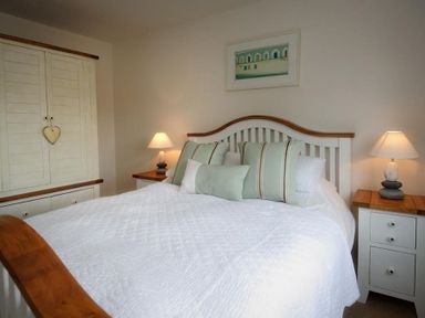 A bedroom with a white bed and green pillows two bedside tables with lamps and a wardrobe at Ty Coed Abersoch