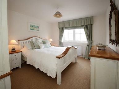A bedroom with a white bed with green pillows bedside tables with lamps a window with curtains and a dresser with a mirror at Ty Coed in Abersoch