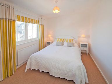 A bedroom with a bed between two bedside tables with lamps and yellow striped curtains at Ty Coed in Abersoch