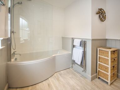 A bathroom with a bathtub shower screen towel warmer and basket storage at Ty Coed in Abersoch