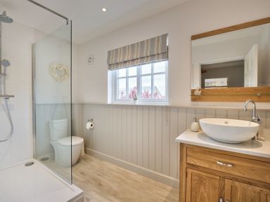 A bathroom with a walk-in shower toilet wooden vanity with a vessel sink and a window with striped blinds at Ty Coed in Abersoch