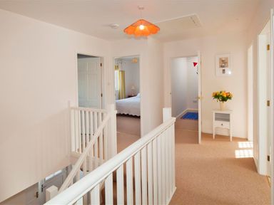 A hallway with carpeted floor white railing a small table with flowers and doors leading to bedrooms at Ty Coed in Abersoch
