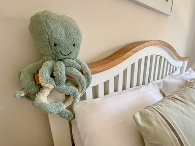 A bed with pillows and a wooden headboard with a plush octopus toy hanging on the side at Ty Coed  in Abersoch